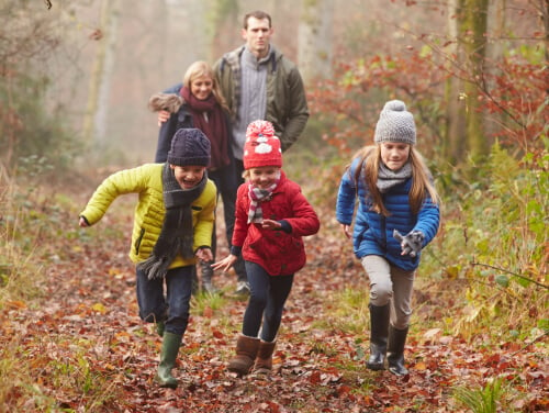 Three children running away from their parents down a forest lane.