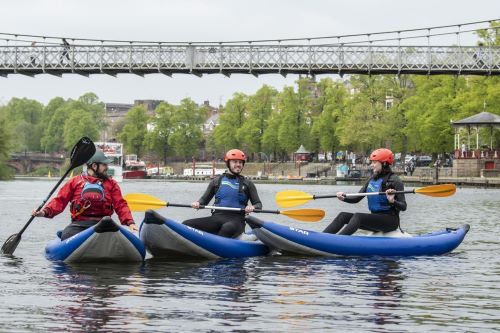 Three people each in their own canoes having a conversation.