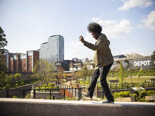 A man walking along a narrow wall in Manchester in the sunshine with a smile on his face