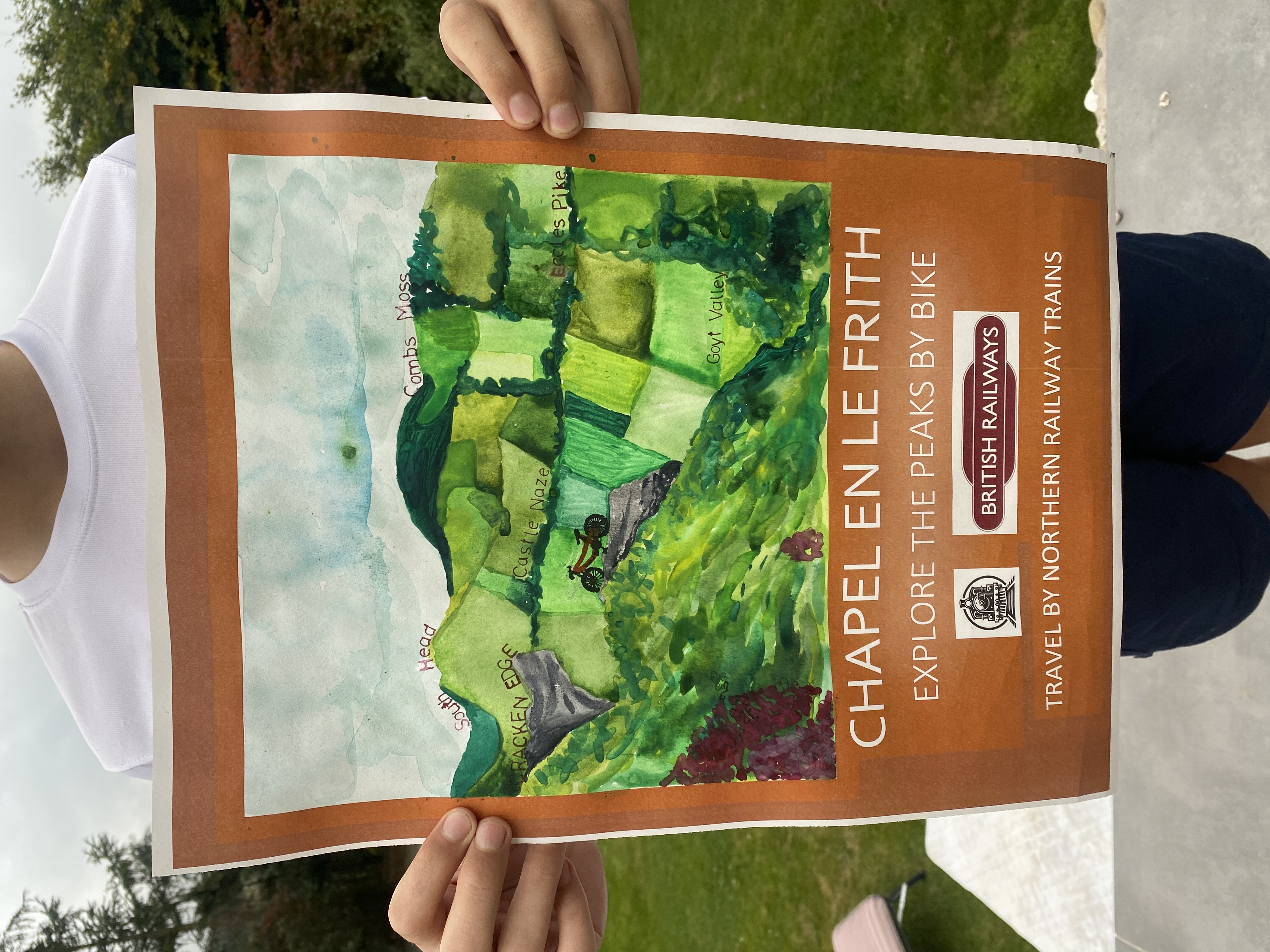 A boy holding up winning artwork. Artwork shows a scenic view of the peaks with green hills and fields.