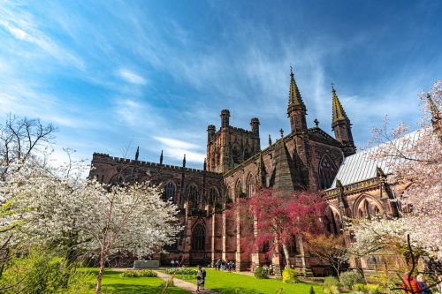 Chester cathedral overlooking the gardens that surround it, there are people walking through the gardens as well.