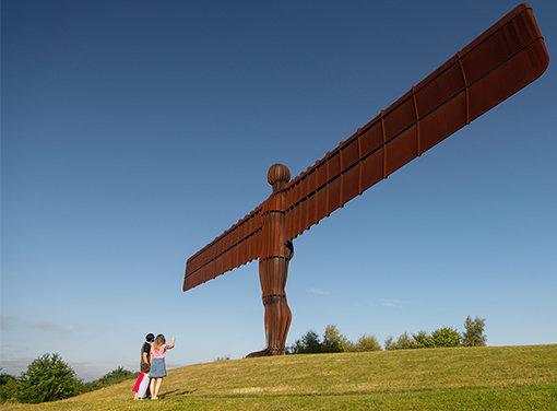 The Angel of the North statue in Manchester with two people standing looking up at it