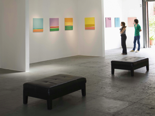 a man and a woman standing in an art gallery looking at pictures.