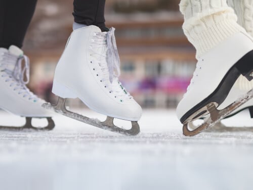 A close up of two people wearing white ice skates on an ice rink