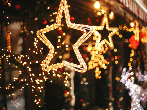 A star made of lights in front of a wreath with another star behind the wreaths.