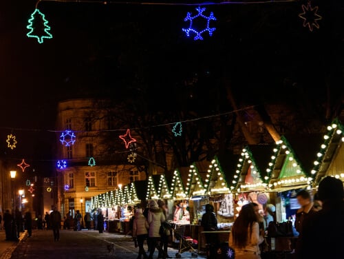 A christmas market in the centre of a town. Each stall is adorned with christmas lights with more lights hanging overhead.