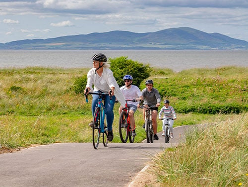 alt="Four adults wearing helmets cycling on a path in the Lake District"