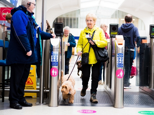 Elderly woman walking through ticket barriers at a train station while walking a dog