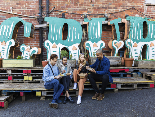 Four adults sitting on wooden palettes to enjoy street food in Manchester