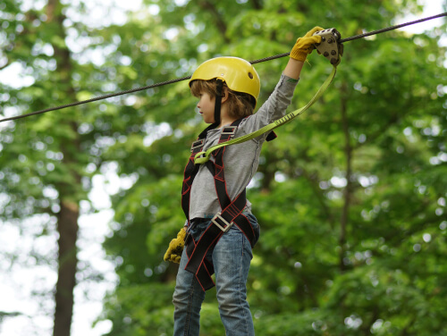 A small child clipped into a harness in the trees at Go Ape