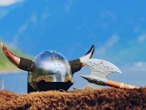 A close-up of a Viking helmet with horns beside an axe