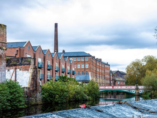 the front of some old factories on kelham island. the sky is overcast and it looks likely to rain. there is a canal in the foreground with a bridge going over it.