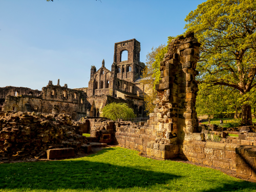 the ruins of Kirkstall Abbey on a sunny day with the highest point looking over trees.