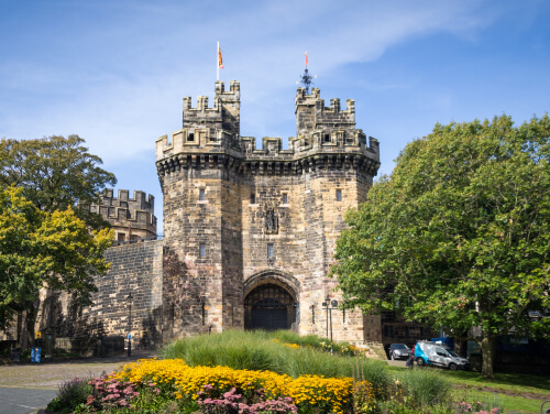 The front gate of a castle looming over the gardens that surround it.