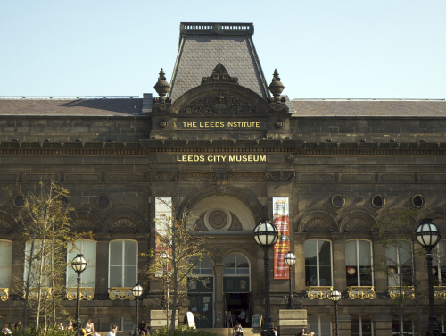 The front façade of Leeds City Museum, framed by two poles with banners on them.