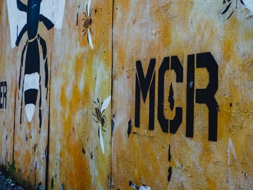 A close-up of a spray painted wall with MCR and a bee on it in Manchester