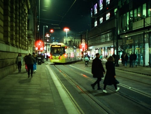 A busy Manchester street at night with a tram incoming