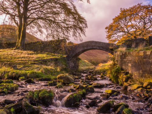 A bridge over a creek that is very shallow with lots of rocks shown through the water. There are old walls on either side of the bridge.