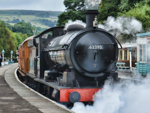 A steam train pulling into a station platform with a lot of steam billowing around it.