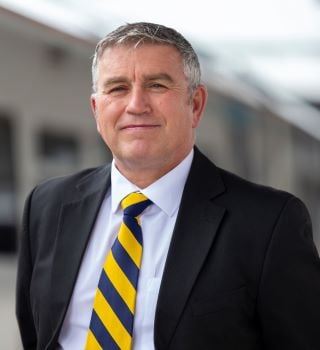 Image of Richard Issac, wearing black suit with white shirt and yellow and blue stripped tie