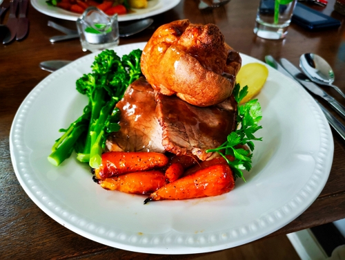 A close-up of a traditional roast dinner with beef, carrots, broccoli and a Yorkshire pudding on top