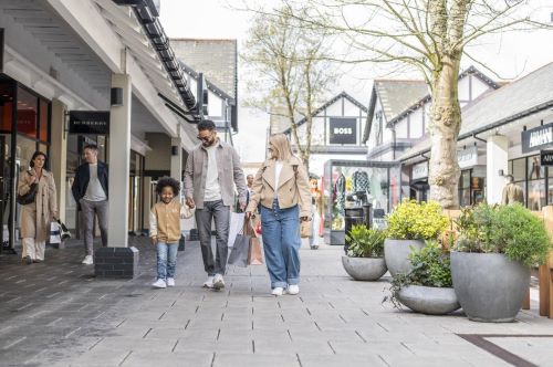 A family walking through the Cheshire Oaks Shopping Centre with other people walking around them. 