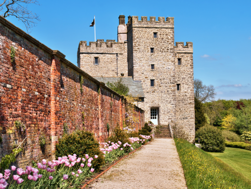 Sizergh Estate on a sunny day, with a gravel path aligned with flowers leading up to it.