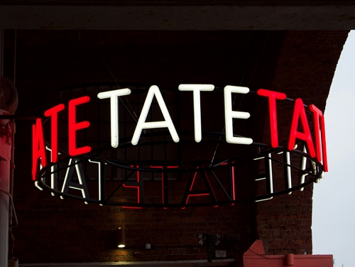 An illuminated sign that says TATE in capitals letters repeated in a circle