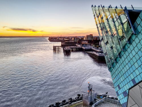 The exterior glass walls of The Deep in Hull beside the water at sunset