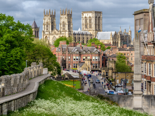 York Minster looming over a bridge with buildings covering the bottom of the minster. The city walls run alongside the bridge.