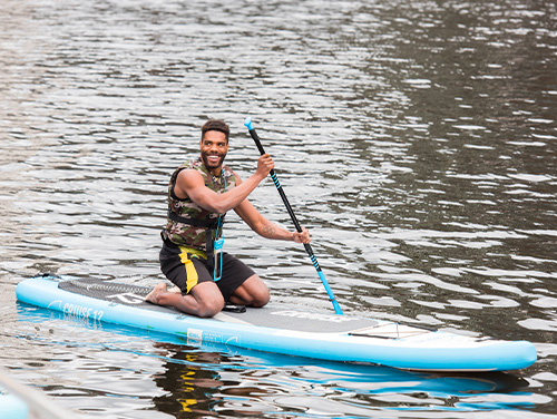 a man on a paddleboard using the paddle to move. He is kneeling on it to retain his balance.