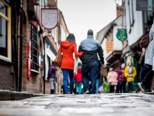 A couple walking down the York Shambles with their backs to the camera. There are people walking around them to the sides.