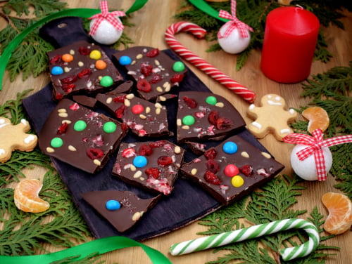 A bar of chocolate white candied chocolate embedded into it broken into multiple pieces all in irregular shapes. there are festive decorations scattered around the bar.