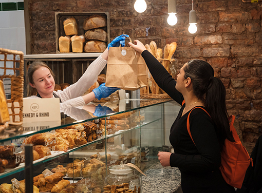 Lady working in a Newcastle bakery passing a brown paper bag over to a female customer