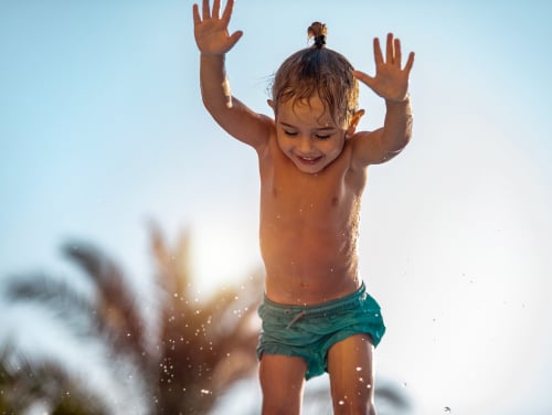 A child playing in the sun and the water laughing and jumping
