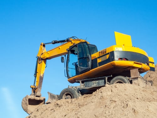 A large digger on a mound of dirt scooping more dirt from below it on a clear sunny day
