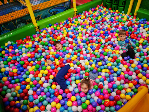 Three kids playing in a large ball pit which is fenced in and part of a larger play area.