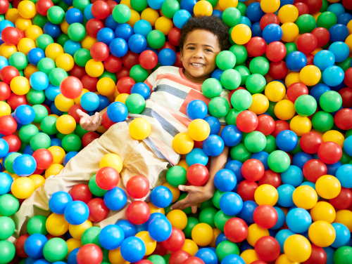 A child partly submerged in a ball pit whilst smiling.