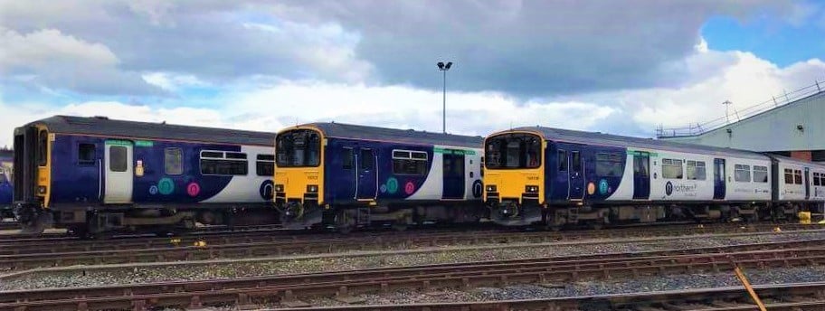 three northern trains are shown behind railway tracks at Newton Heath train station