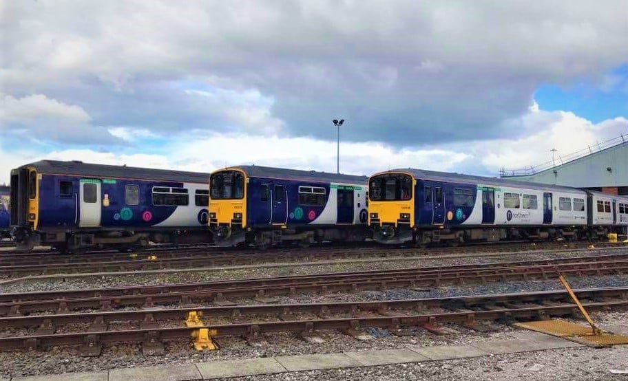 three northern trains are shown behind railway tracks at Newton Heath train station